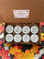 An open brown cardboard gift box labeled 'Fall Discovery Box' filled with shredded paper and eight small round metal tins. The tins have white labels with autumn-themed names including 'Manderley Estate', 'Book Witch', 'Slee
py Hollow', and others.
