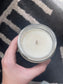 Hand holding a small jar of white candle against a patterned fabric background