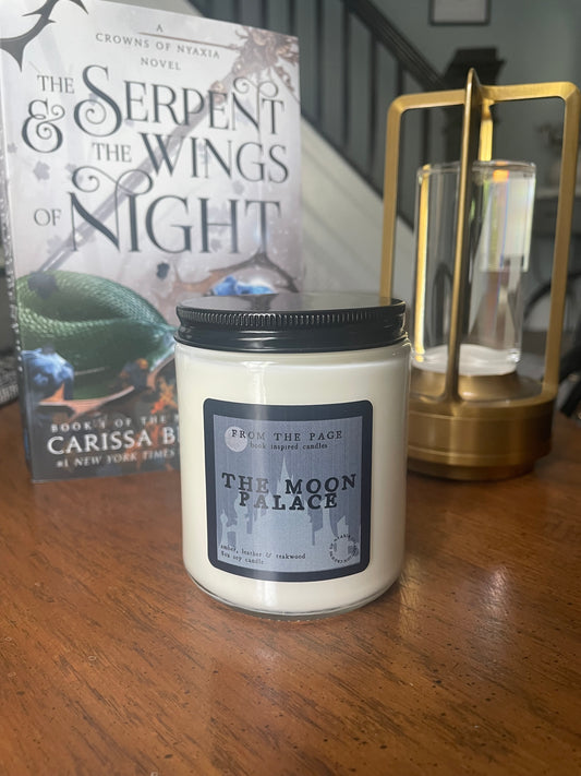 Candle with a label on a wooden surface next to a book titled 'Serpent and the Wings of Night'.